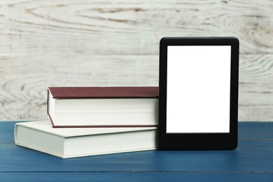 Photo of Portable e-book reader and hardcover books on blue wooden table, space for text