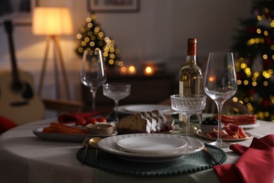 Photo of Christmas table setting with bottle of wine, appetizers and dishware in room