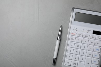 Calculator and pen on grey table, top view. Space for text