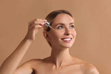 Beautiful woman applying cosmetic serum onto her face on beige background