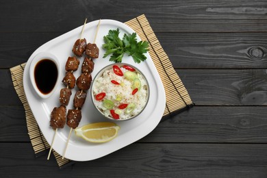 Tasty chicken meat glazed in soy sauce served with rice on black wooden table, top view. Space for text