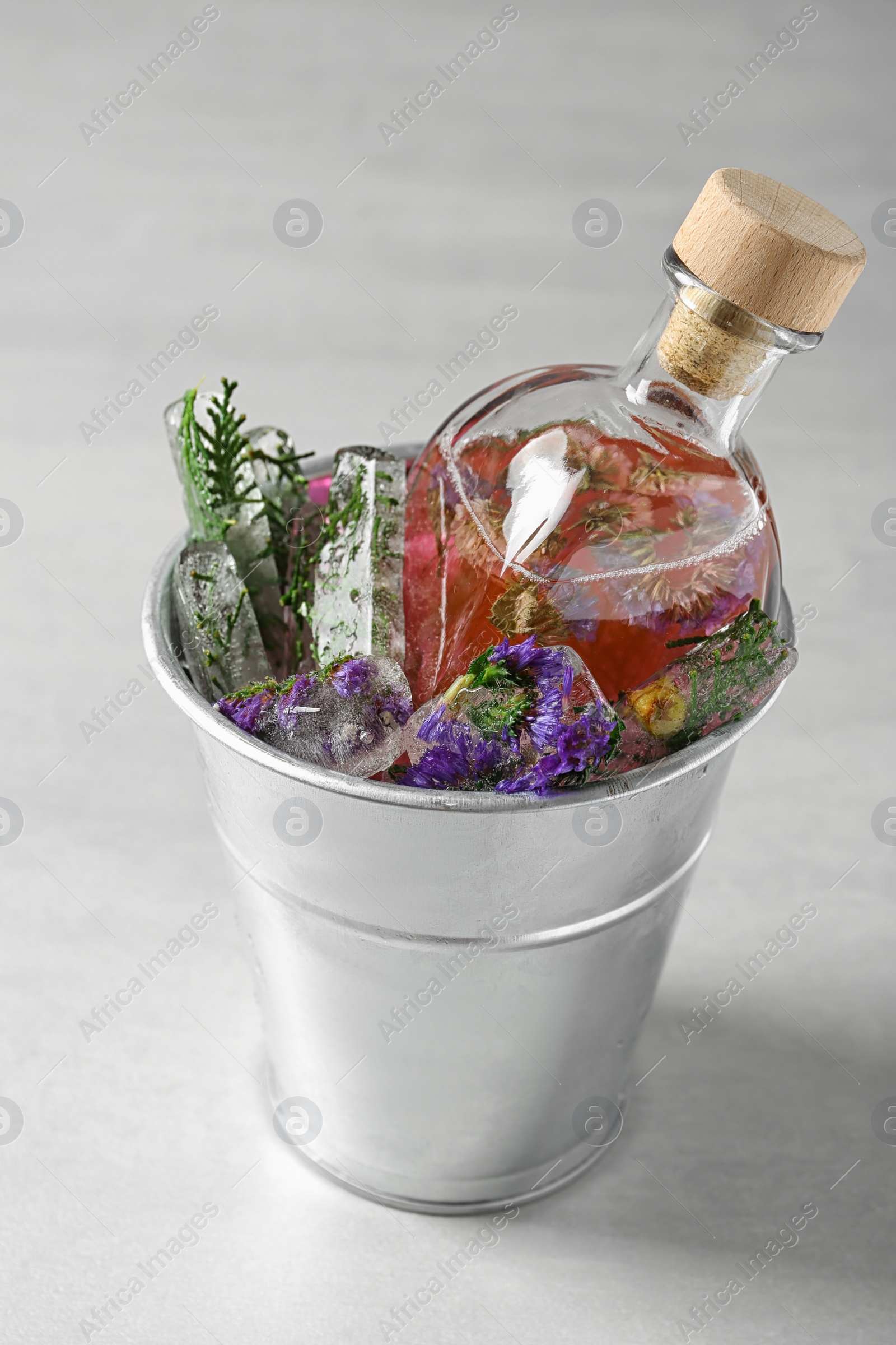 Photo of Bucket of ice cubes with flowers and glass bottle on light table