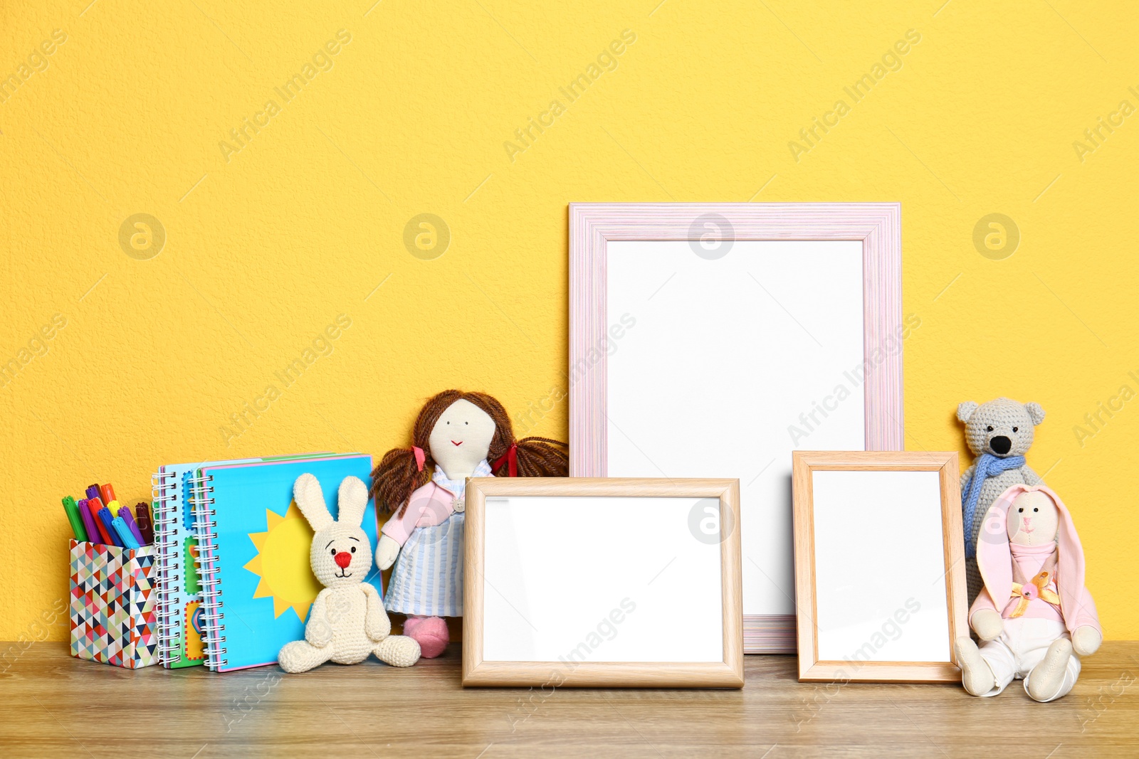 Photo of Soft toys and photo frames on table against yellow background, space for text. Child room interior