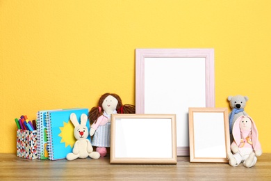 Photo of Soft toys and photo frames on table against yellow background, space for text. Child room interior