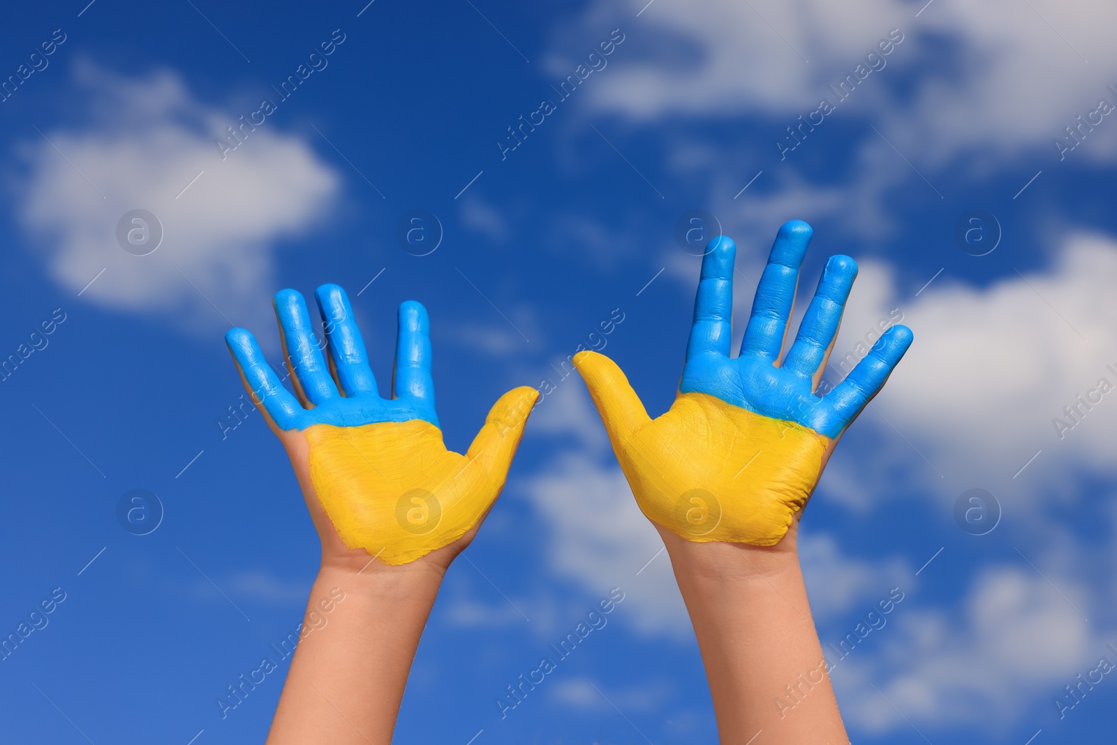 Photo of Little girl with hands painted in Ukrainian flag colors against blue sky, closeup. Love Ukraine concept