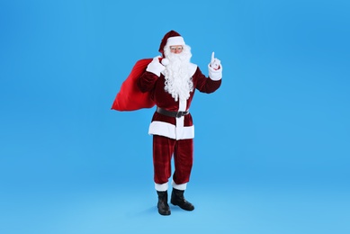 Photo of Full length portrait of Santa Claus with sack on light blue background