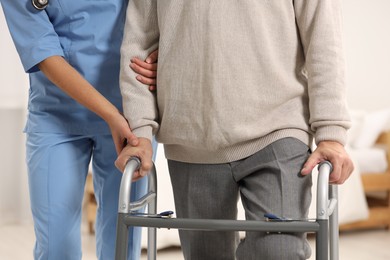 Nurse helping elderly patient with walker indoors, closeup