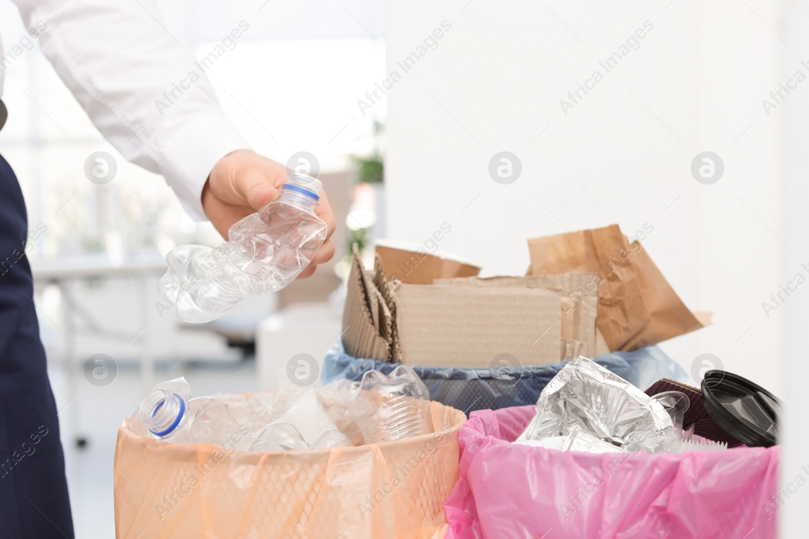 Photo of Man putting used plastic bottle into trash bin in office, closeup. Waste recycling
