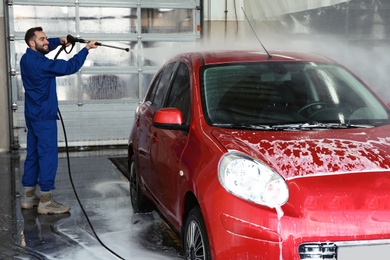 Worker cleaning automobile with high pressure water jet at car wash