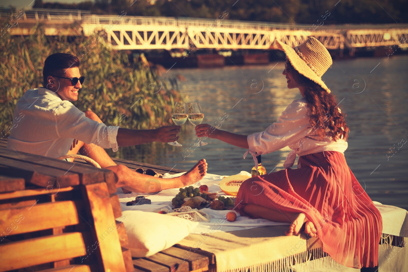 Photo of Couple clinking glasses with wine on pier at picnic