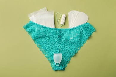 Photo of Panties, menstrual cup and other hygienic products on light green background, flat lay