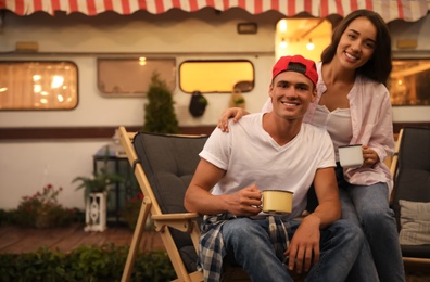 Photo of Happy couple with cups resting on deck chairs near motorhome. Camping season