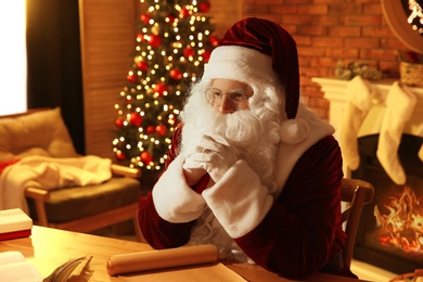 Photo of Santa Claus with wish list at table indoors