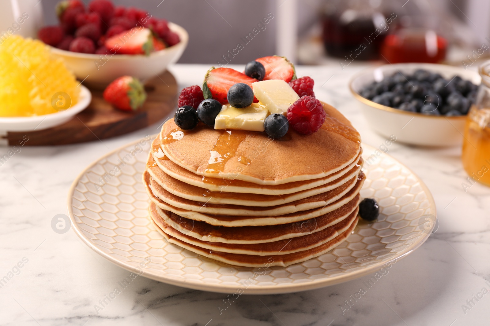 Photo of Delicious pancakes with fresh berries, butter and honey on white marble table, closeup