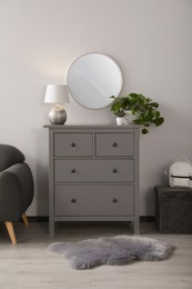 Photo of Stylish room interior with round mirror on wall over chest of drawers