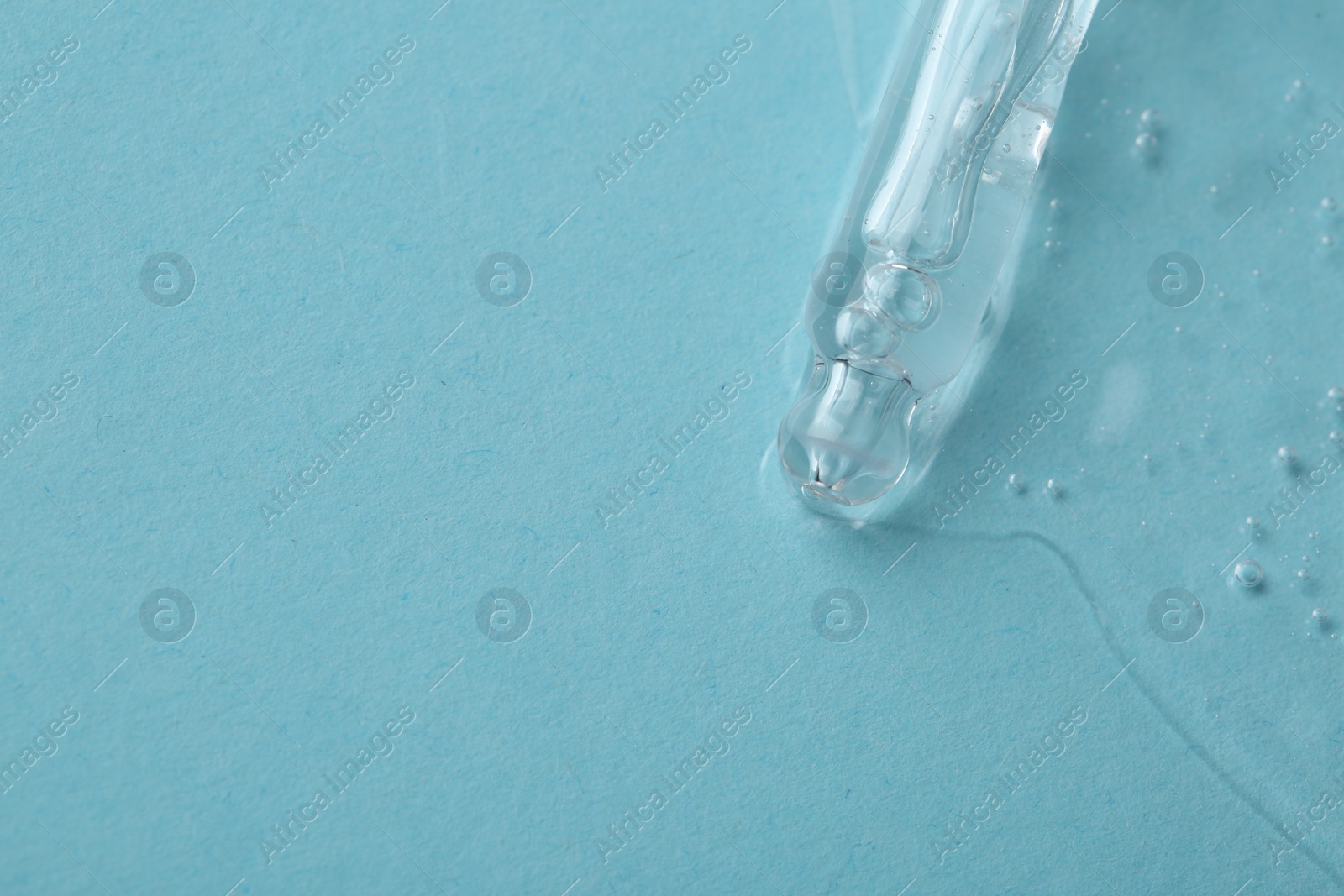 Photo of Dripping cosmetic serum from pipette onto light blue background, top view. Space for text