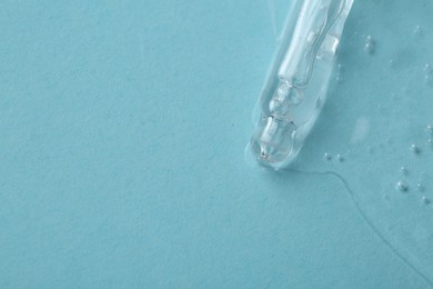 Photo of Dripping cosmetic serum from pipette onto light blue background, top view. Space for text
