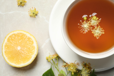 Cup of tea, lemon and linden blossom on light grey marble table, flat lay