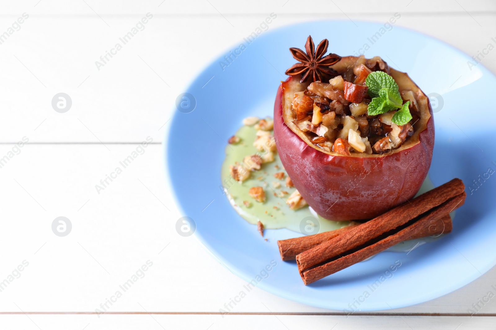 Photo of Tasty baked apple with nuts, honey, spices and mint on white wooden table, space for text