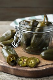 Photo of Board with pickled green jalapeno peppers on wooden table