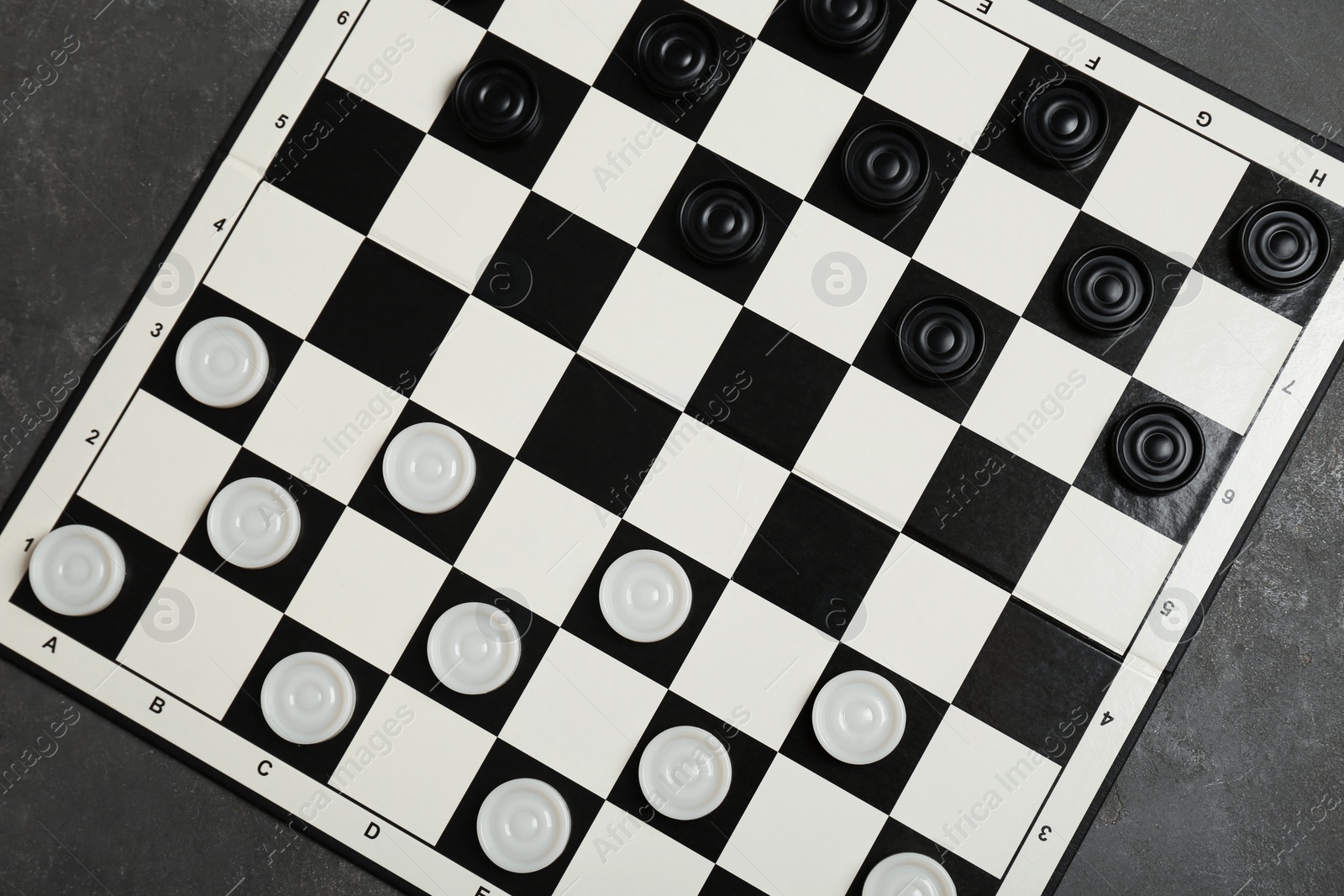 Photo of Checkerboard with game pieces on grey table, top view