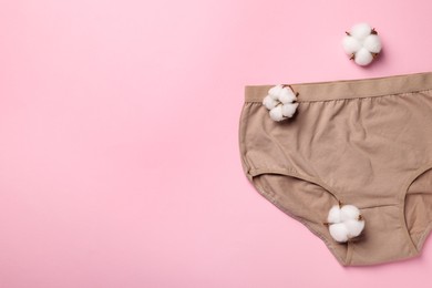 Beige women's underwear and cotton flowers on pink background, flat lay. Space for text