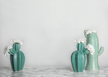 Photo of Trendy cactus shaped vases with flowers on table against light wall. Creative decor