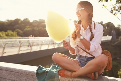 Young woman with cotton candy outdoors on sunny day. Space for text