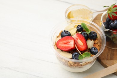 Photo of Tasty granola with berries, yogurt and almond flakes in plastic cup on white table. Space for text