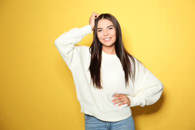 Happy young woman wearing warm sweater on yellow background 