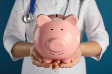 Photo of Doctor holding piggy bank on blue background, closeup. Medical insurance