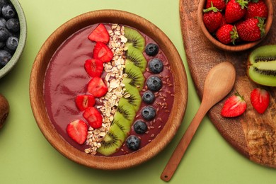 Photo of Bowl of delicious smoothie with fresh blueberries, strawberries, kiwi slices and oatmeal on light green background, flat lay