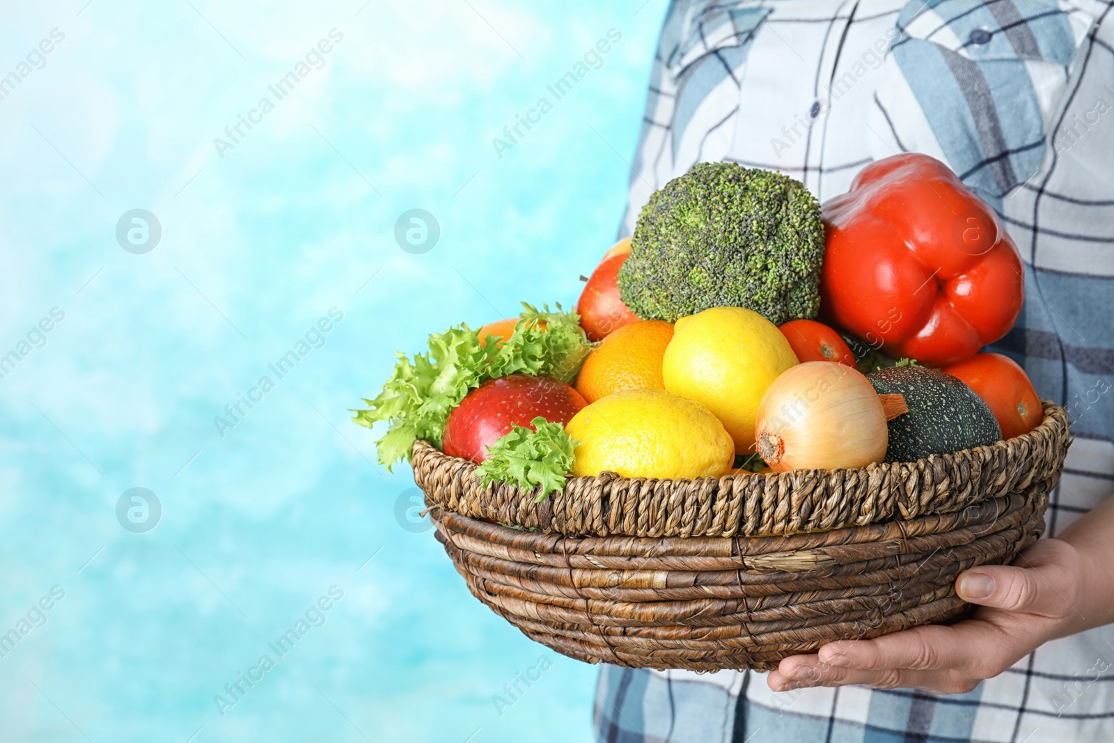 Photo of Woman holding wicker bowl with ripe fruits and vegetables on color background, closeup. Space for text