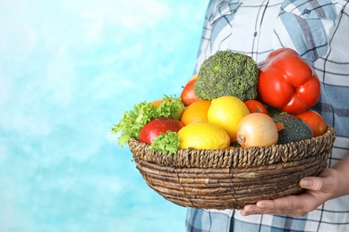 Photo of Woman holding wicker bowl with ripe fruits and vegetables on color background, closeup. Space for text