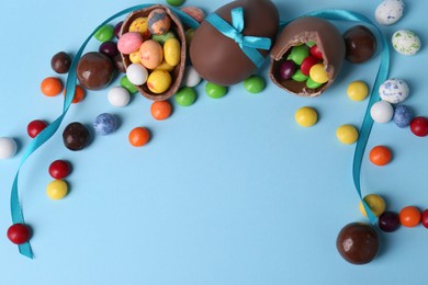 Composition with tasty chocolate eggs and different candies on light blue background, above view. Space for text