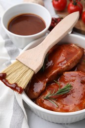 Photo of Raw marinated meat, rosemary and basting brush on table, closeup