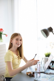 Photo of Cute teenage blogger with laptop and different cosmetics at table