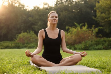 Photo of Beautiful woman practicing yoga on mat outdoors. Lotus pose