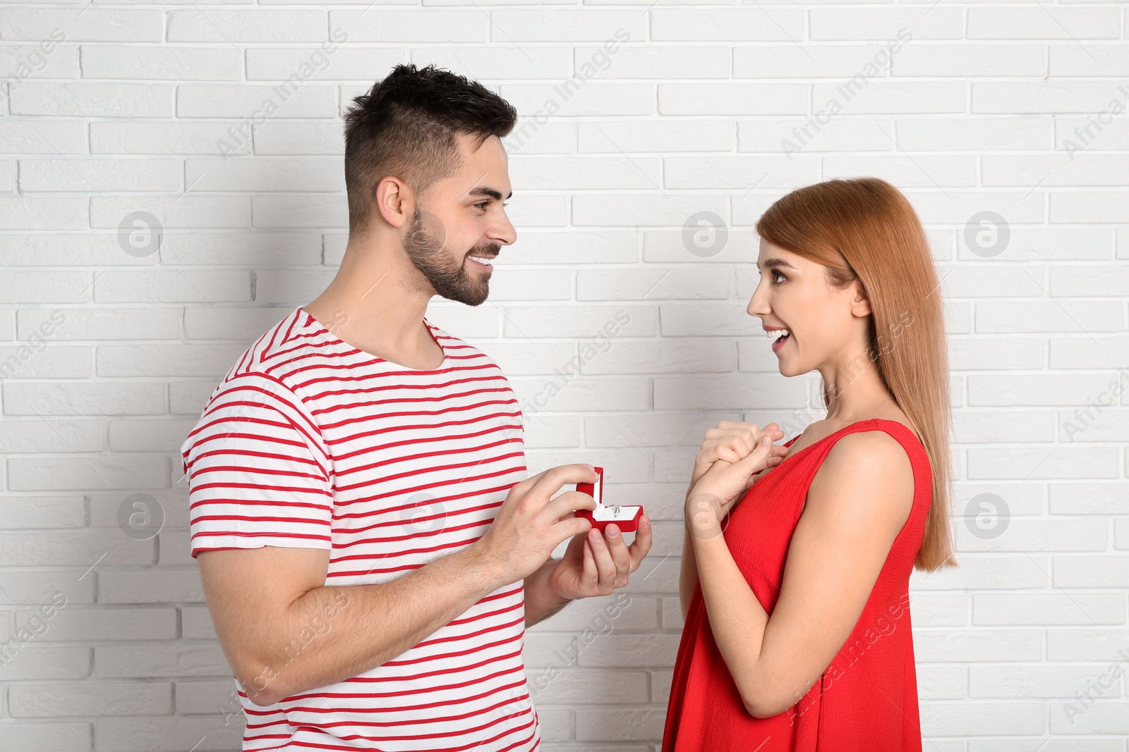 Photo of Man with engagement ring making marriage proposal to girlfriend near white brick wall