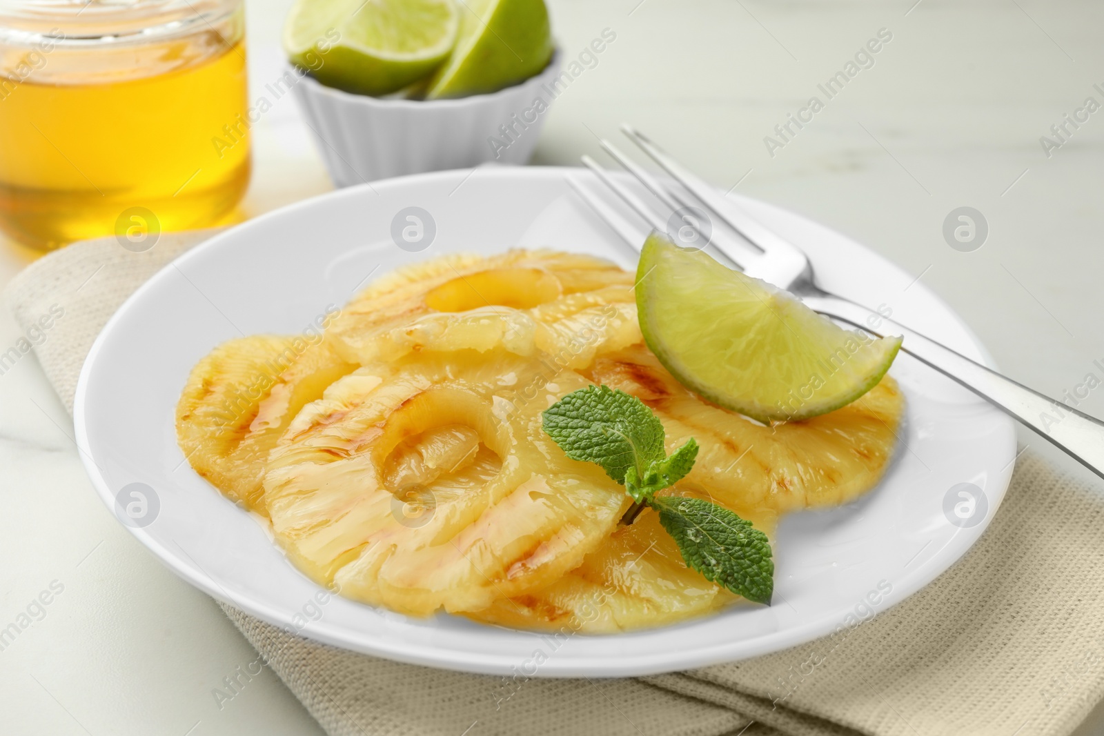 Photo of Tasty grilled pineapple slices, piece of lime and mint on white table, closeup