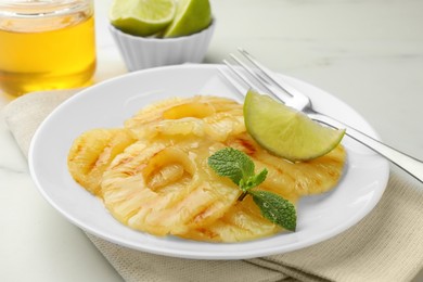 Tasty grilled pineapple slices, piece of lime and mint on white table, closeup