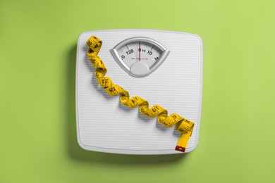 Scales and measuring tape on green background, top view. Weight loss concept