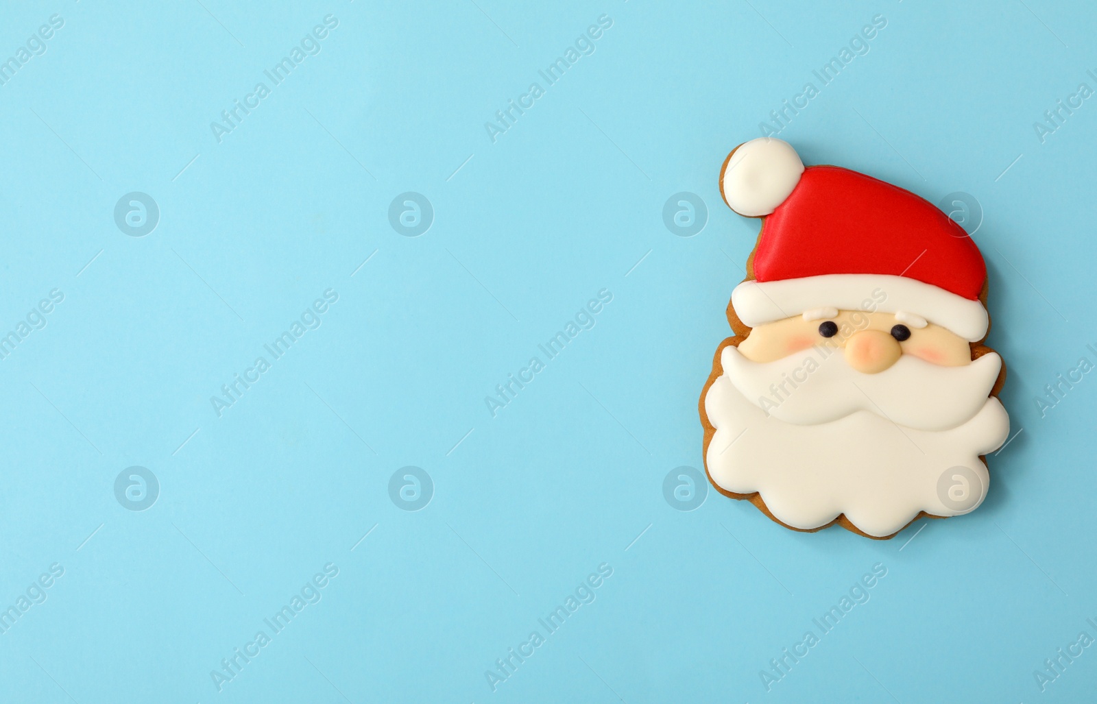 Photo of Christmas Santa Claus face shaped gingerbread cookie on light blue background, top view. Space for text