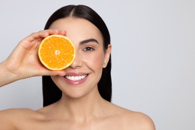 Woman holding half of orange on light grey background, space for text. Spa treatment