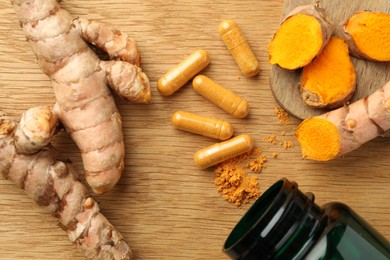 Photo of Aromatic turmeric powder, raw roots and pills on wooden table, flat lay