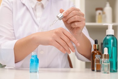 Photo of Dermatologist testing cosmetic product at white table indoors, closeup