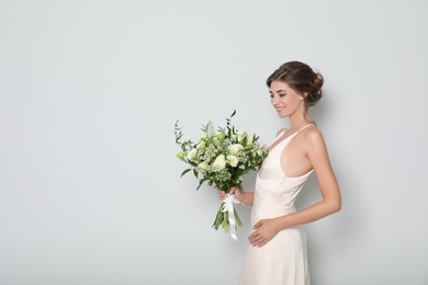 Young bride wearing wedding dress with beautiful bouquet on light grey background. Space for text