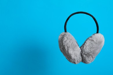 Stylish winter earmuffs on light blue background, space for text