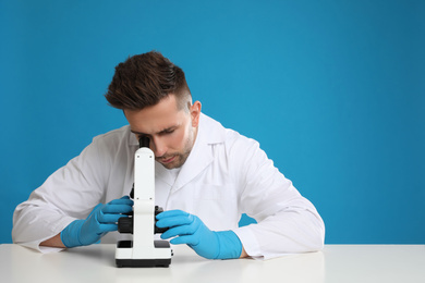 Scientist using modern microscope at table against blue background. Medical research