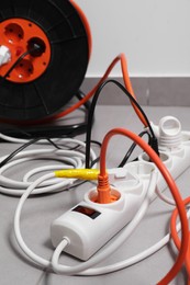Extension cord reel plugged into power strip on grey floor indoors, closeup